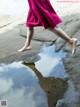 A woman in a pink dress is walking on a puddle of water.