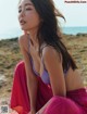 A woman in a purple bikini sitting on a beach.